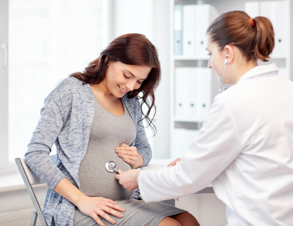 A medical professional uses a stethoscope to examine the abdomen of a pregnant woman during a checkup.
